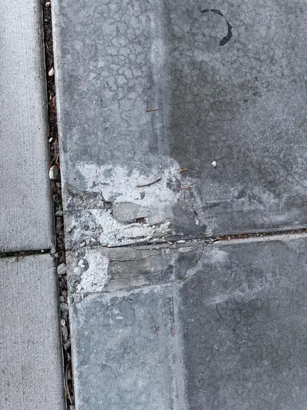 Worn concrete slab with scaling, spalled patches and fine map cracking along a joint
