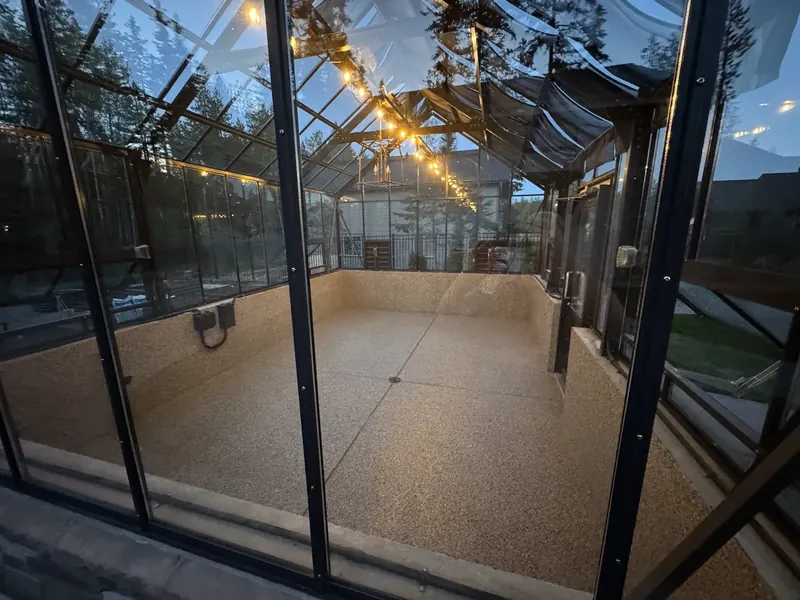 Tan flake coating on the floor of a glass greenhouse at dusk, string lights overhead